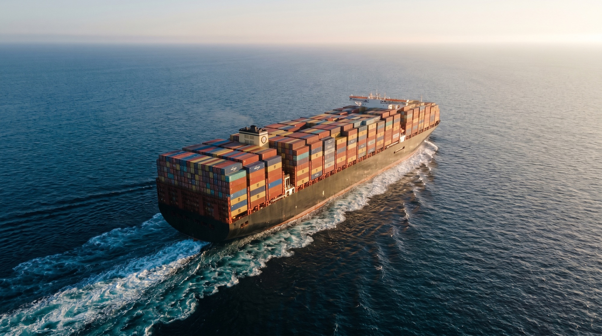 A large commercial container ship underway in open ocean at golden hour